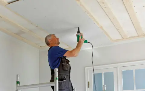 Man spacklar med remsa i taket, skruvar gipsskivor på träreglar.