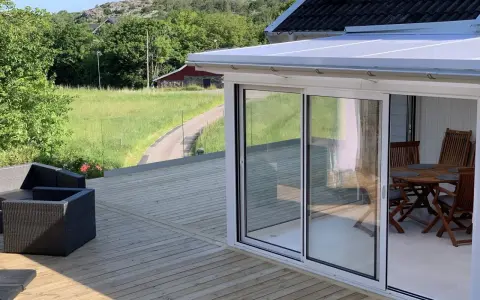 Nybyggd veranda med glaspartier och tak, perfekt för att bygga en mysig uteplats. Utsikt över grönskande landskap.