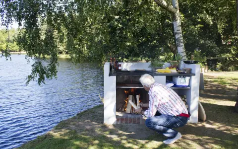 Man tänder en murad grill vid en sjö.