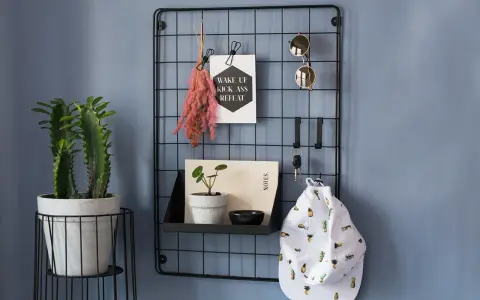 En inreda hall med en växt, en svart gallervägg med solglasögon, nycklar, en hatt med ananasmönster och en inspirerande poster.
