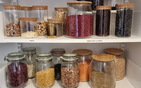 Välordnat skafferi med glasburkar fyllda med nötter, torkad frukt, frön och baljväxter. Perfekt för att organisera skafferi.