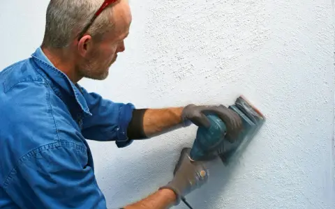 Man slipar en vägg med en excenterslip för att få bort slipdamm innan målning.