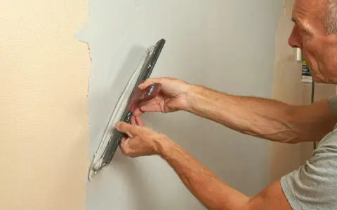 En man använder tapetsera verktyg för att jämna ut spackel på en vägg.