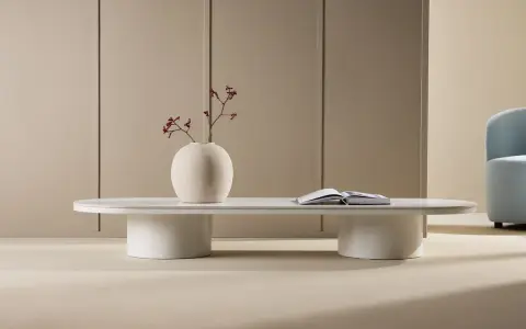 Ett stilrent, ovalt soffbord i vitt med en rund vas med torkade blommor och en öppen bok.
