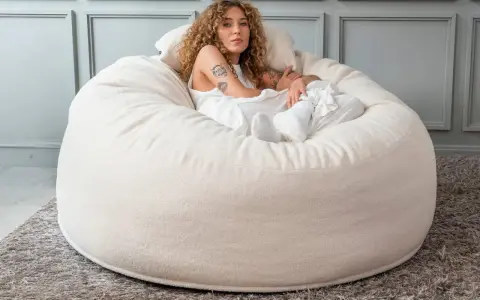 En kvinna med lockigt hår vilar i en stor, mjuk beige sittpall.