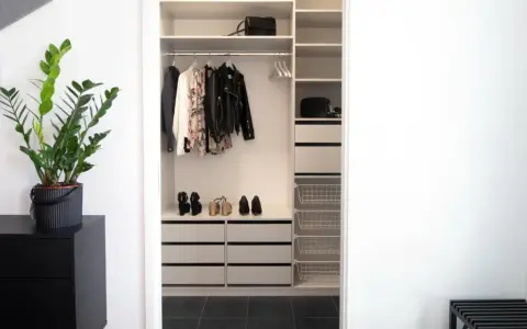 En stilren liten walk in closet med kläder, skor och väskor. En grön växt på en svart byrå ger liv.
