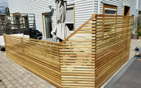 Nybyggt staket i trä ramar in uteplatsen. Grillen och parasollet syns bakom.