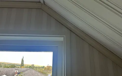 Takskena i snedtak med panelklädda väggar. Fönstret ger utsikt över hus och höstfärgad natur.