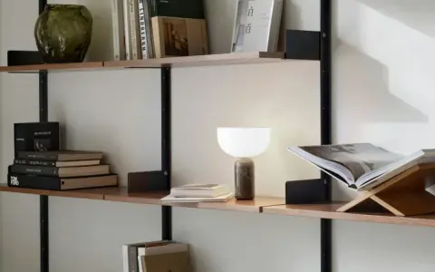 En stilren hylla i vardagsrummet med böcker, en vas och en lampa.