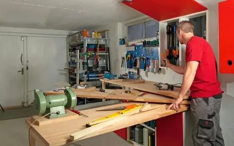 Man i röd tröja i en inredd verkstad. Verktyg på väggen, bänkar med maskiner och material.
