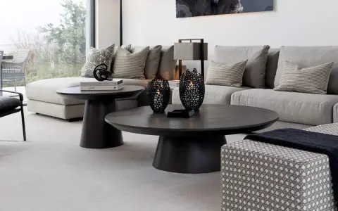 Ett modernt vardagsrum med en stor, mörk soffa och ett elegant, runt soffbord. Två svarta ljuslyktor står på soffbordet.