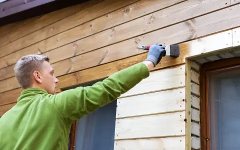 Man målar panel utomhus med pensel. Träet får en varmare ton.