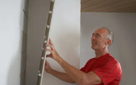 Man tapetserar på gipsskiva med ett leende.