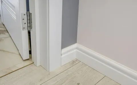 Nymålade vita snickerier runt en dörröppning och längs väggen. Golvet är ljust träliknande laminat.