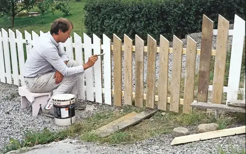 Man målar ett vitt staket. En burk med färg står bredvid.