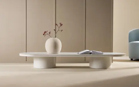 Ett modernt, ovalt soffbord med en vit puff-liknande bas. En vas med en gren och en öppen bok står på bordet.