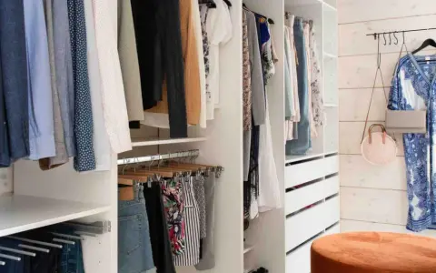 En walk-in closet med kläder på galgar, lådor och en blåvit klänning på väggen.