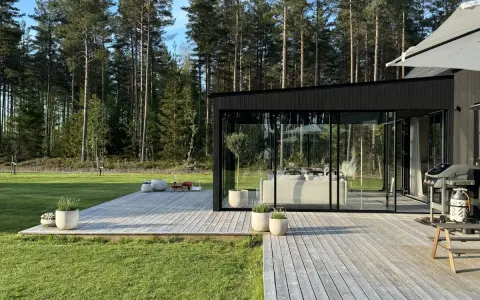 Enkel uteplats med trätrall och glaspartier som vetter mot en grönskande skog. Perfekt för avkoppling.