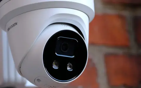 Vit övervakningskamera med Hikvision-logotyp, monterad mot en tegelvägg. Ger trygghet med larmklass 1.