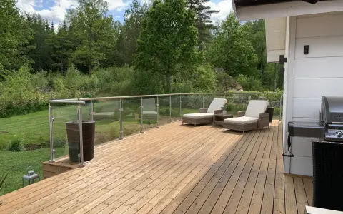 Nyligen oljad altan med solstolar och grill. Vacker utsikt över grönskande skog.