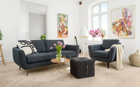 En modern soffgrupp 3+2 i mörkblått tyg, med en fåtölj, soffbord, pall och konst på väggarna.
