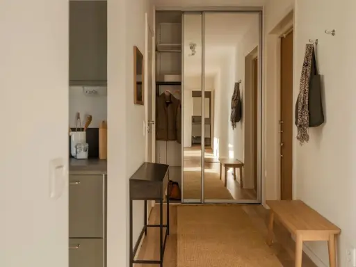 En ljus och inbjudande vit hall med en spegelgarderob, en smal konsol och en bänk. En matta i jute ger värme.