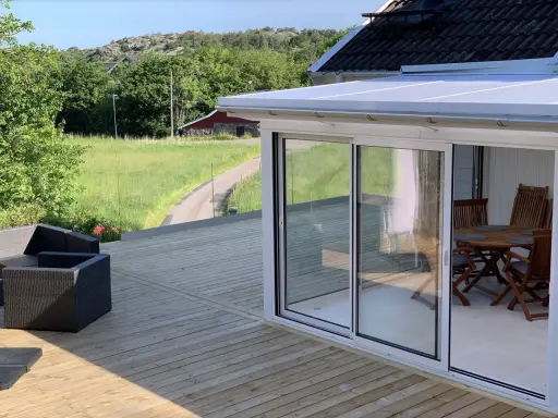 Nybyggd veranda med glaspartier och tak, perfekt för att bygga en mysig uteplats. Utsikt över grönskande landskap.