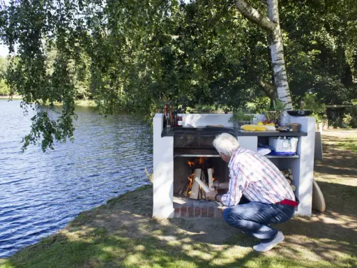 Man tänder en murad grill vid en sjö.