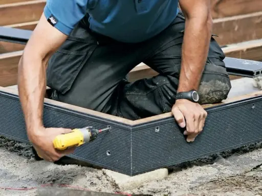 Byggare skruvar fast en mörk komposittrall. Ett vanligt problem med komposittrall är att den kan vara svår att få perfekt jämn.