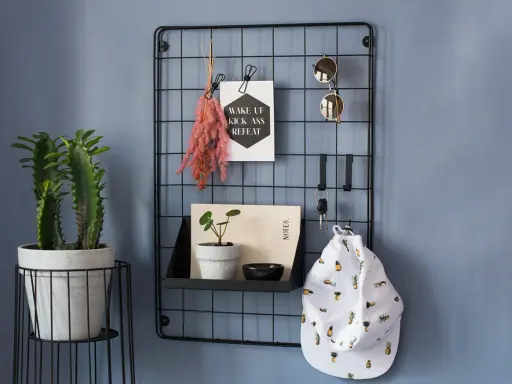En inreda hall med en växt, en svart gallervägg med solglasögon, nycklar, en hatt med ananasmönster och en inspirerande poster.