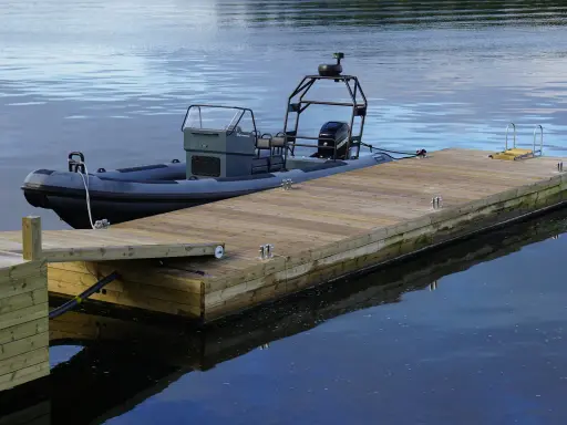 En nybyggd brygga med en mörkgrå RIB-båt förtöjd. Perfekt för att njuta av sommaren vid vattnet.