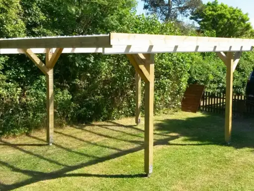En nybyggd carport på plintar står på en gräsmatta. Träkonstruktionen har ett tak av plast eller metall.