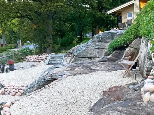 En vacker uteplats sten med grusgångar, stenmurar och en trappa som leder upp mot ett hus.