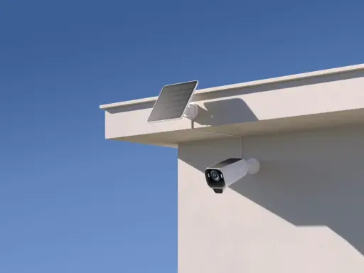 En eufycam 2 pro test visar en vit övervakningskamera med solpanel monterad på en vit vägg under en blå himmel.