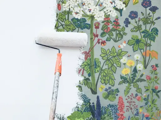 En färgroller målar över en blommig tapet.
