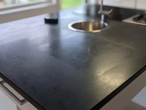 En mörk stenskiva med diskho och kran. Ytan ser ut att vara nybehandlad, som efter att man valt att slipa stenskiva för att ge den nytt liv.