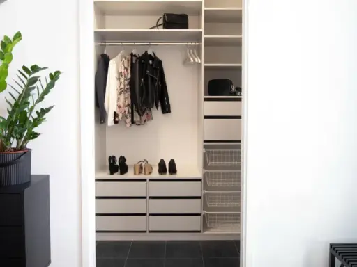 En stilren liten walk in closet med kläder, skor och väskor. En grön växt på en svart byrå ger liv.