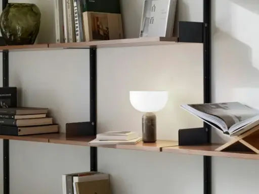 En stilren hylla i vardagsrummet med böcker, en vas och en lampa.