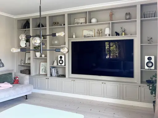 En platsbyggd bokhylla i vardagsrummet med en stor TV i mitten. Hyllorna är fyllda med böcker, dekorationer och växter.