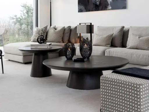 Ett modernt vardagsrum med en stor, mörk soffa och ett elegant, runt soffbord. Två svarta ljuslyktor står på soffbordet.