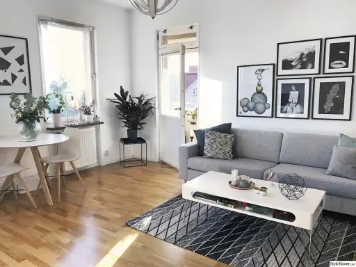 Mysig etta med grå soffa, vitt soffbord och en rund matplats. Konst på väggarna ger personlighet.