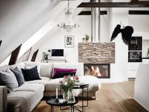 Mysigt vardagsrum med öppen spis, soffa och ett soffbord i 3 delar med blommor och ljus.