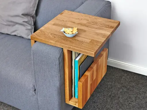 Ett smart diy soffbord i trä som hängs över armstödet på en grå soffa. Perfekt för att förvara böcker och ha en skål med kex nära till hands.