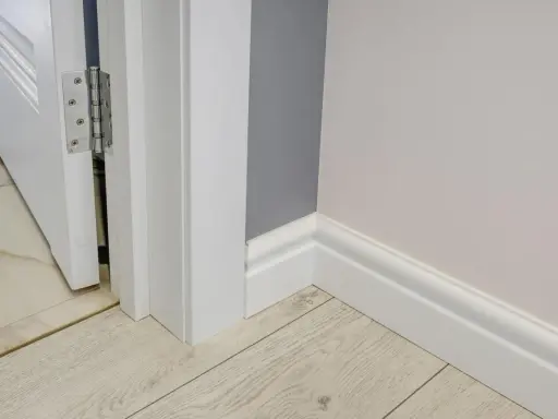 Nymålade vita snickerier runt en dörröppning och längs väggen. Golvet är ljust träliknande laminat.
