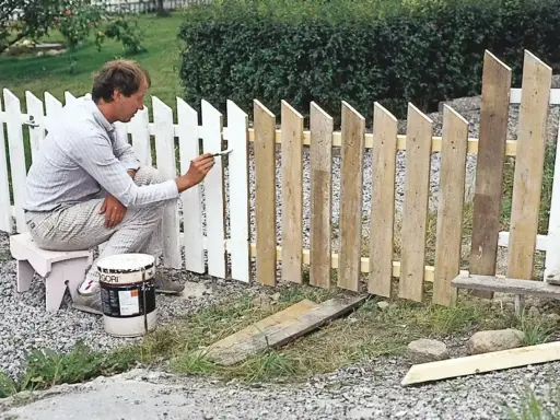 Man målar ett vitt staket. En burk med färg står bredvid.