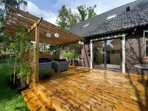 Träaltan med pergola och loungegrupp ger härlig altan inspiration. Solrosor och grönska ramar in.