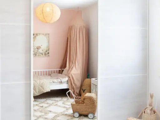 A child's closet with clothes and baskets, a pink bedroom with a bed and canopy, and a white wall with a window.