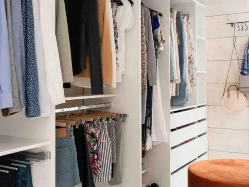 En walk-in closet med kläder på galgar, lådor och en blåvit klänning på väggen.