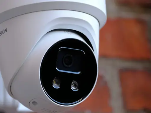 Vit övervakningskamera med Hikvision-logotyp, monterad mot en tegelvägg. Ger trygghet med larmklass 1.