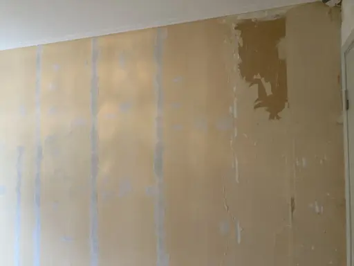 En vägg med gul tapet som lossnat på flera ställen, med synliga limrester och sprickor.